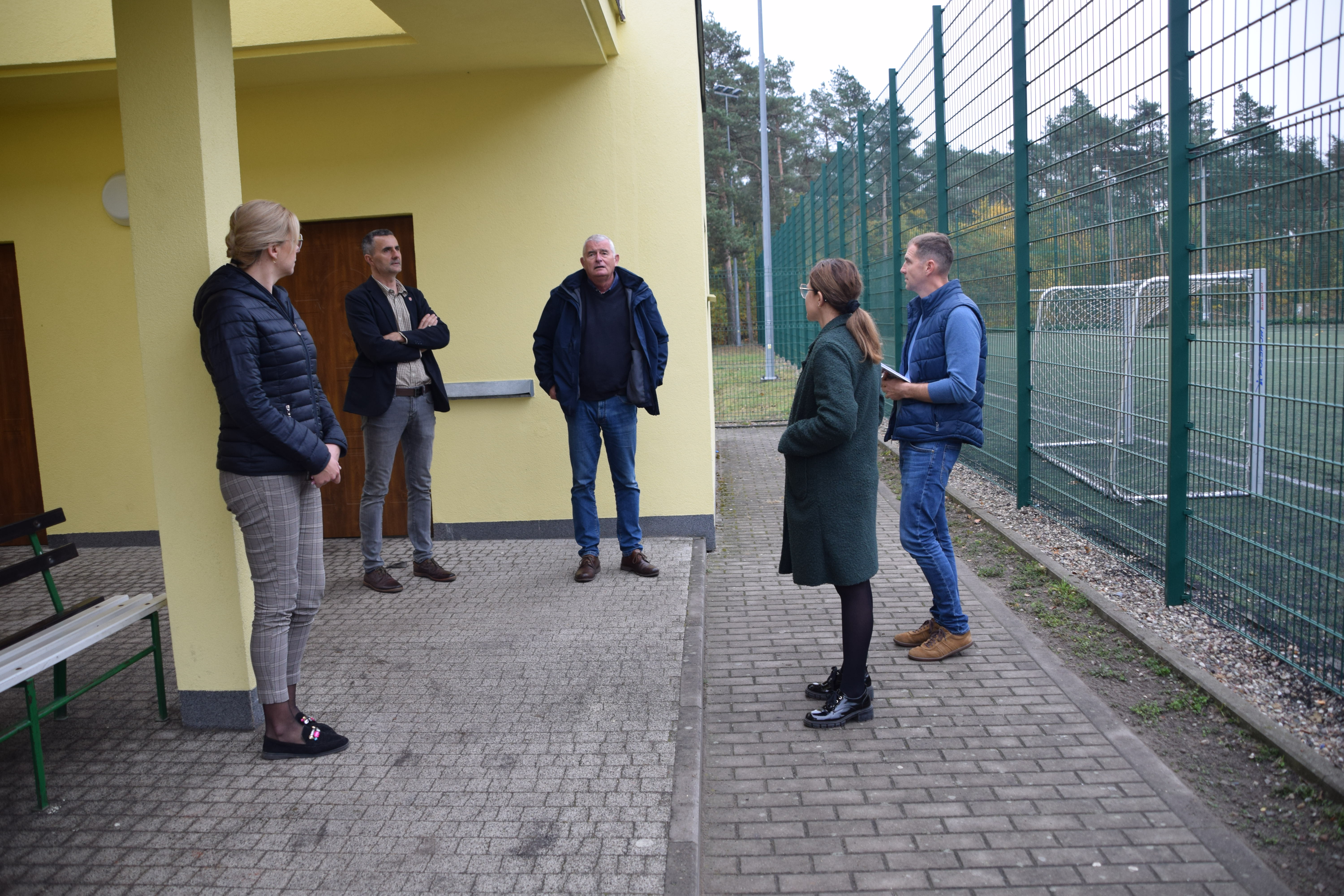 wizytacja przedstawicieli Departamentu Sportu i&nbsp;Turystyki z&nbsp;Urzędu Marszałkowskiego w&nbsp;Poznaniu na&nbsp;zdjęciu W&oacute;jt Gminy Ryczyw&oacute;ł, Kierownik Referatu Inwestycji i&nbsp;Rozwoju Natalia Janus, pracownik urzędu Żaneta Mielcarek stoją przed wyremontowanym budynkiem kompleksu sportowego
