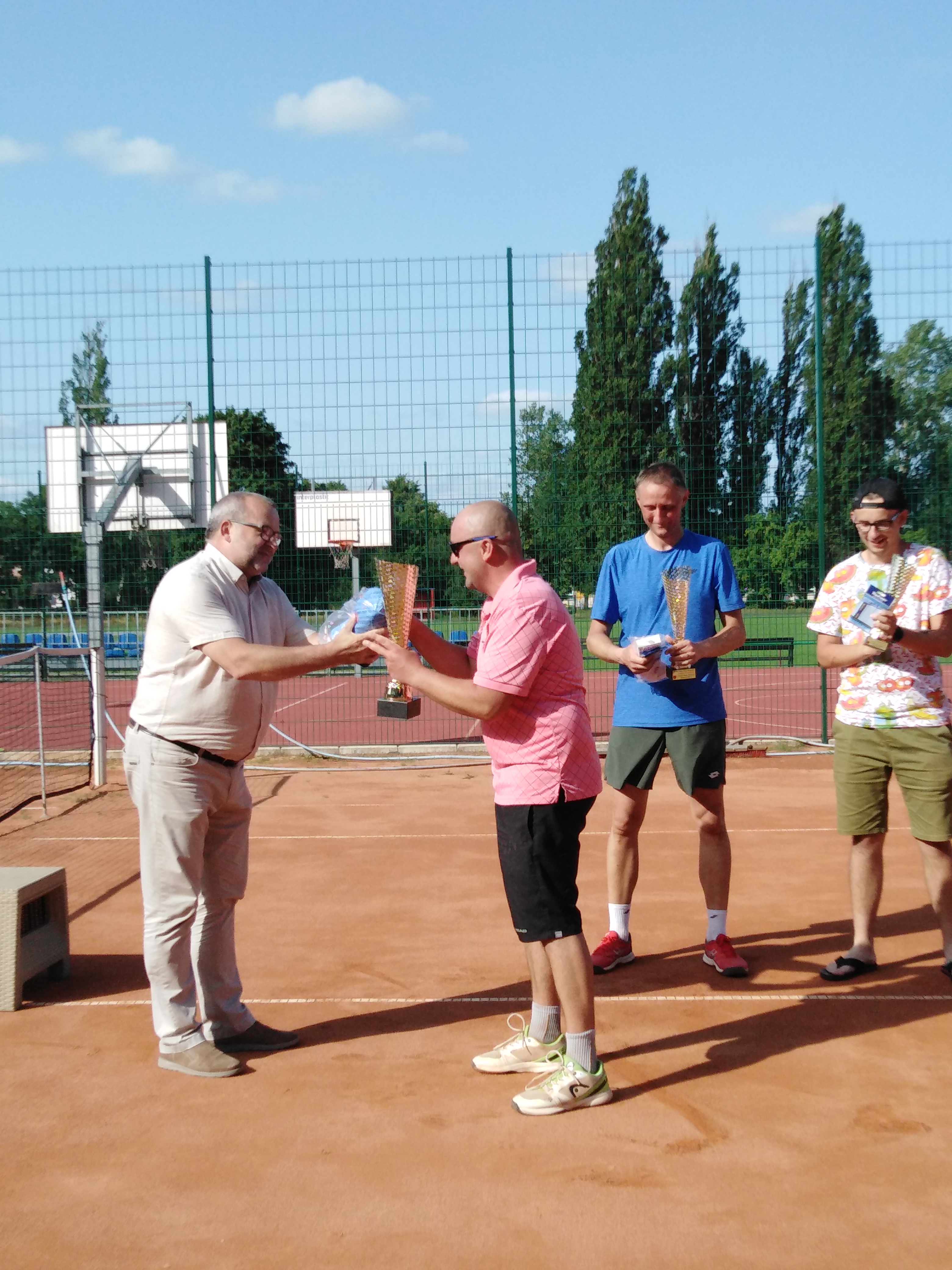 zdjecie przedstawia Wójta Gminy Ryczywół wręczającego puchar za zjaęcie pierwszego miejsca w turnieju tenisa ziemnego p. Dariuszowi Łata w tle widac pozostałych zawodników p. grzegorza Berndt oraz Adama Grabowskiego